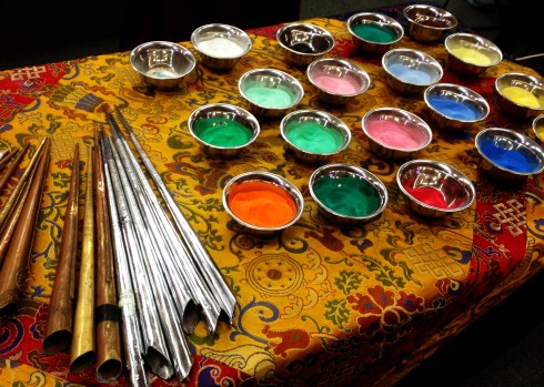 silver cups of colored sand, silver and copper horns nearby, used to gently sift colors onto the curlicues and filagrees of the mandala's expanding circle. 